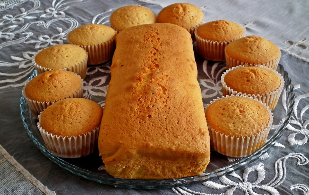 Na szklanym talerzu leży babka piaskowa prostokątna, wokół piaskowe babeczki